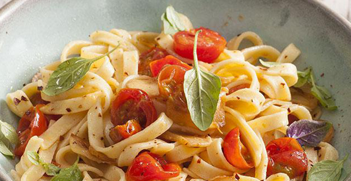 um prato de macarrão com tomates e folhas