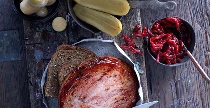 um pires preto com cebola, um pires cinza com um pepino cortado ao meio, um pote cinza com pimenta e uma colher e uma travessa com pão australiano e lombo