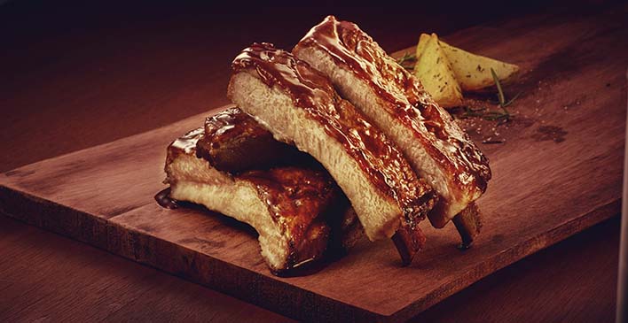 uma tábua de madeira com batatas, alecrim e pedaços de costela suína