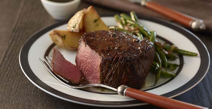 prato branco com listras pretas com batata, aspargos, um bife cortado e um garfo