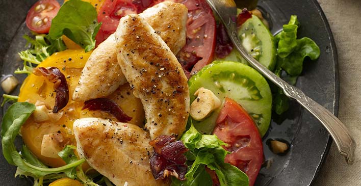 um prato preto com tomates, alfaces, filé de frango frito e um garfo