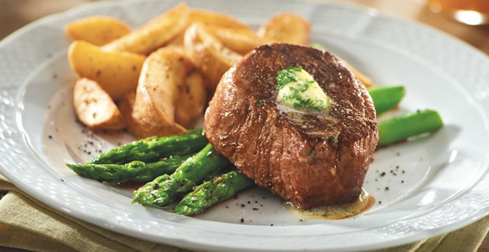 prato branco com batatas rusticas, aspargos e um pedaço de bife