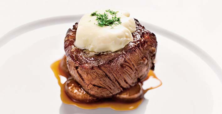 Prato branco um um pedaço de bife em cima de cogumelos e em cima do bife tem um creme branco