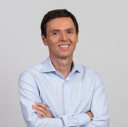 João Campos com uma camisa social azul sorrindo para a câmera em um fundo branco