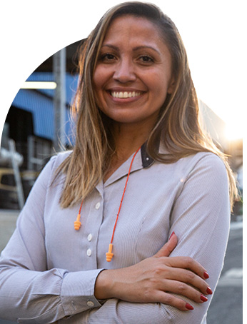 mulher de cabelos loiros sorrindo com earplugs pendurado no pescoço e camiseta social branco azulada