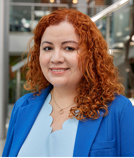 Red-haired woman smiling in a blue blazer and light top.
