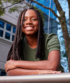 Black woman with braids smiling leaning on a metal bar.
