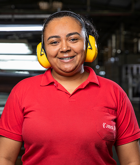 Woman smiling in red JBS polo shirt and yellow earmuffs.