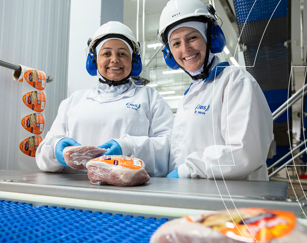 Two smiling women in a JBS factory holding packaged meat.