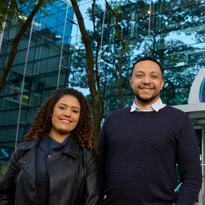 Man and woman smiling in front of a mirrored commercial building.