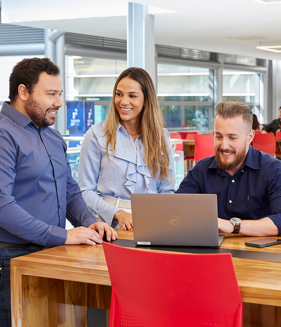 Three smiling professionals in a casual meeting with a laptop.