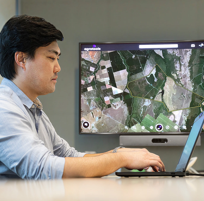 Man using laptop with agricultural satellite map on background screen.