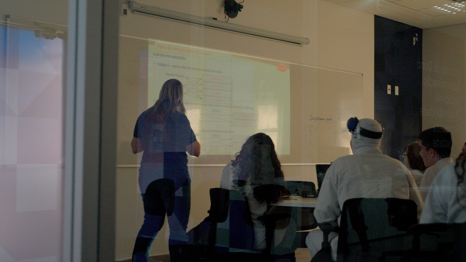 Instrutora apresentando slides sobre custeio em sala.