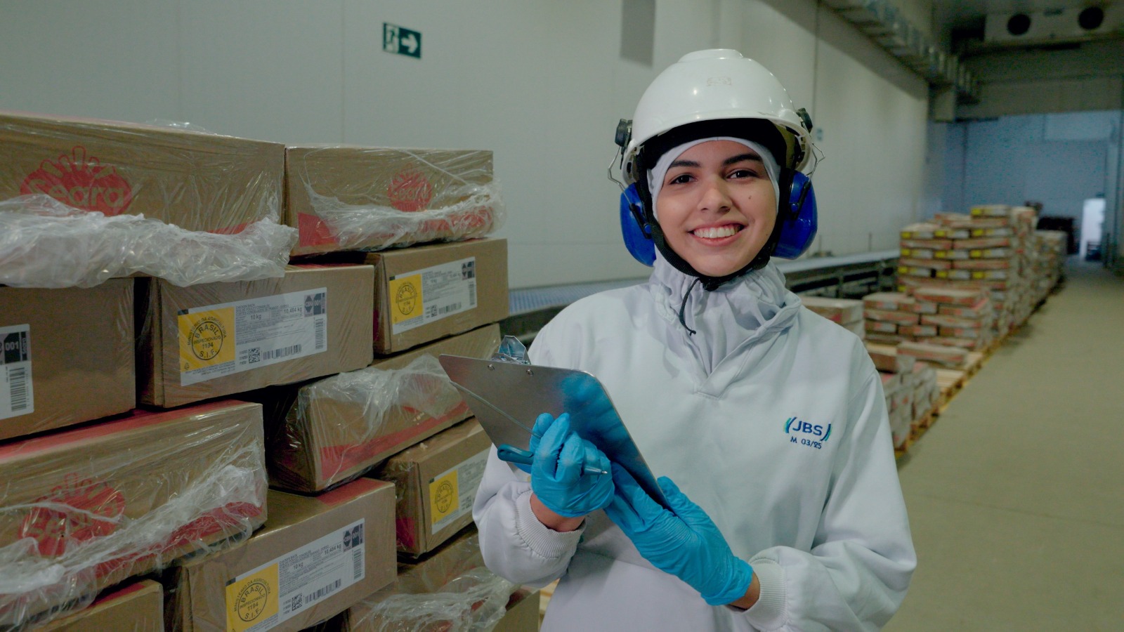 Funcionária sorridente de EPI em armazém com caixas.