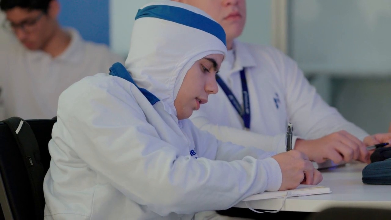 Aluna de uniforme de proteção escrevendo em caderno.
