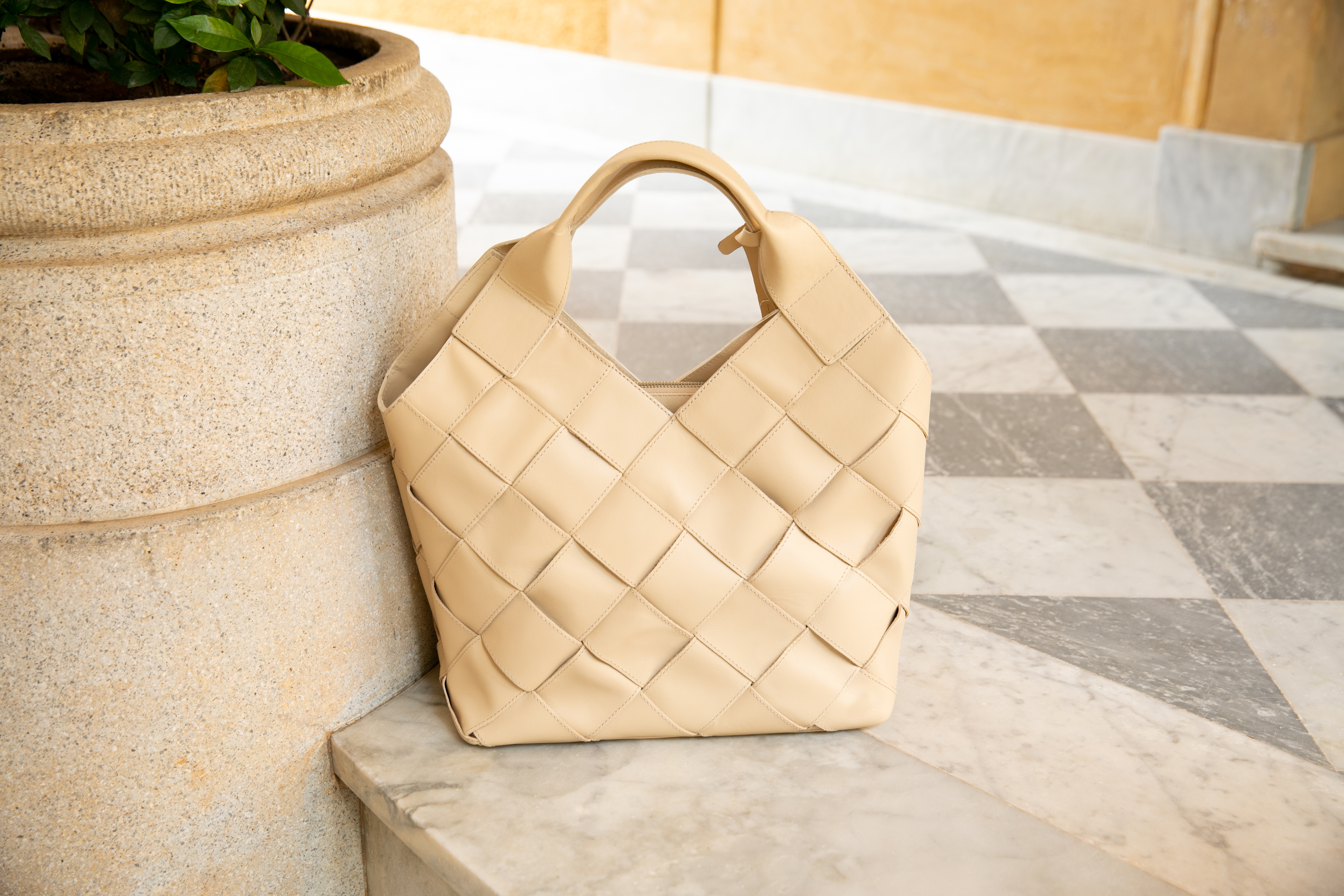 bolsa feita em couro de coloração clara sobre piso marmorizado ao lado de vaso