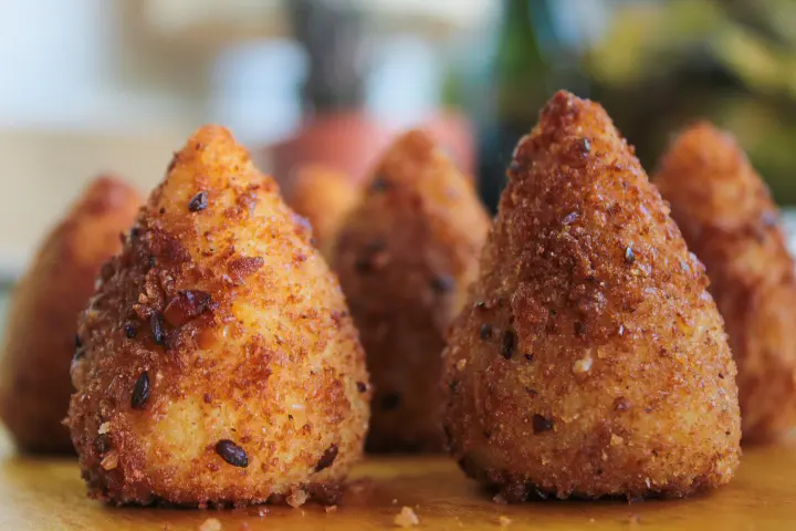 Cinco unidades de coxinha já preparadas sobre uma mesa